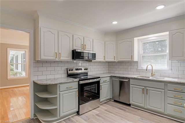 kitchen with appliances with stainless steel finishes, gray cabinetry, plenty of natural light, light stone countertops, and ornamental molding
