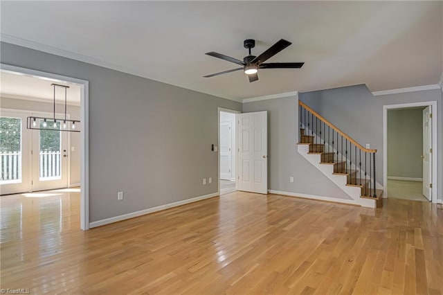 empty room with stairs, ornamental molding, light wood finished floors, ceiling fan, and baseboards