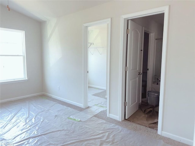 unfurnished bedroom featuring a walk in closet, a closet, light colored carpet, and baseboards