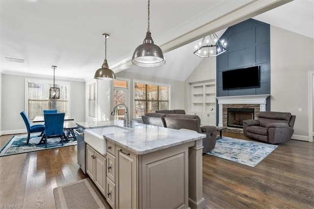 kitchen with a kitchen island with sink, hanging light fixtures, sink, dark hardwood / wood-style floors, and light stone counters