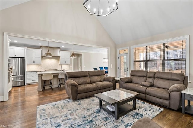 living room with a notable chandelier, wood-type flooring, and high vaulted ceiling