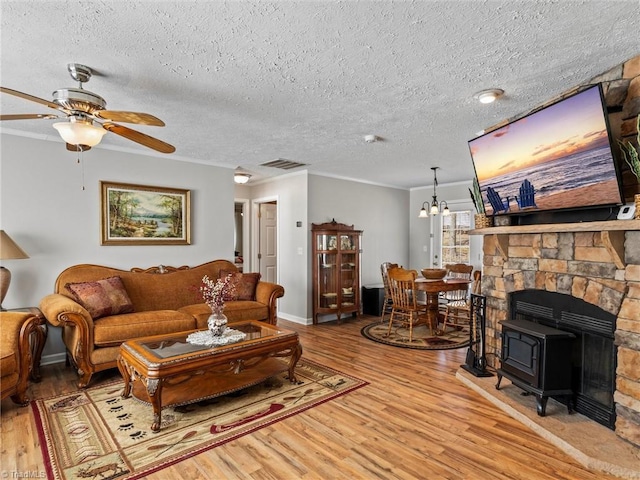 living room with a textured ceiling, ceiling fan with notable chandelier, wood finished floors, visible vents, and ornamental molding