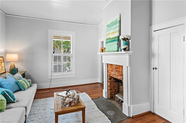 living room with wood finished floors, a brick fireplace, baseboards, and ornamental molding