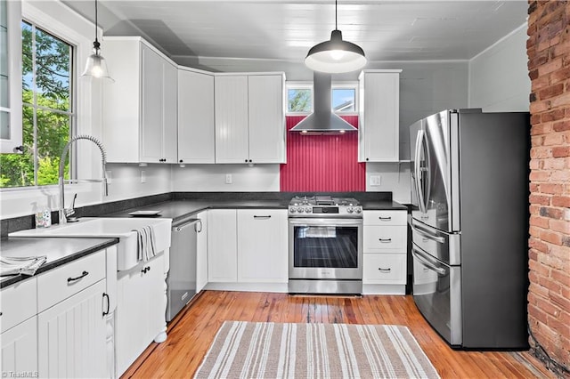 kitchen featuring stainless steel appliances, wall chimney range hood, dark countertops, light wood finished floors, and brick wall
