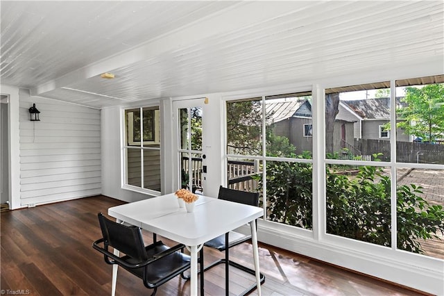 sunroom with plenty of natural light, wood finished floors, wooden walls, and outdoor dining space