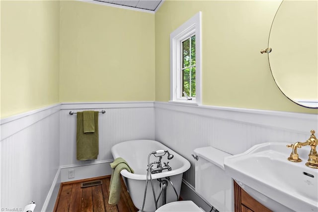 bathroom with a wainscoted wall, a freestanding tub, wood finished floors, toilet, and vanity
