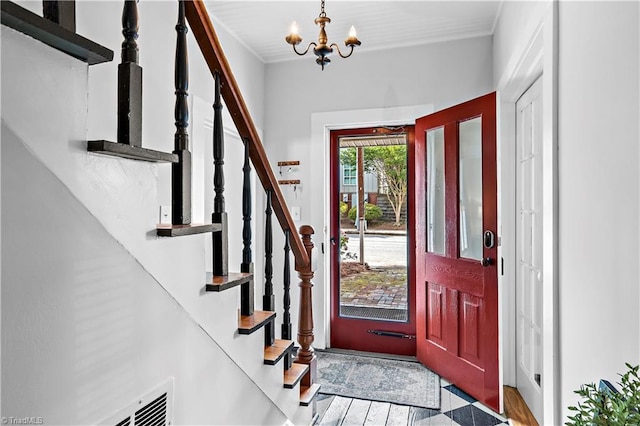 foyer with a chandelier, wood finished floors, stairs, and crown molding