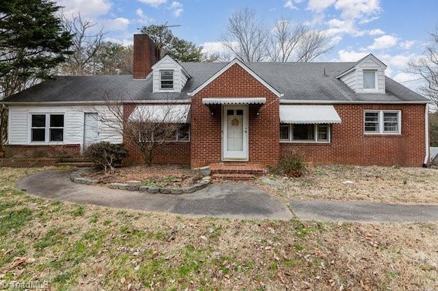 cape cod home with brick siding and a chimney