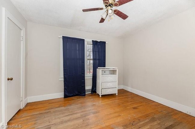 unfurnished bedroom with a textured ceiling, wood finished floors, baseboards, and ceiling fan