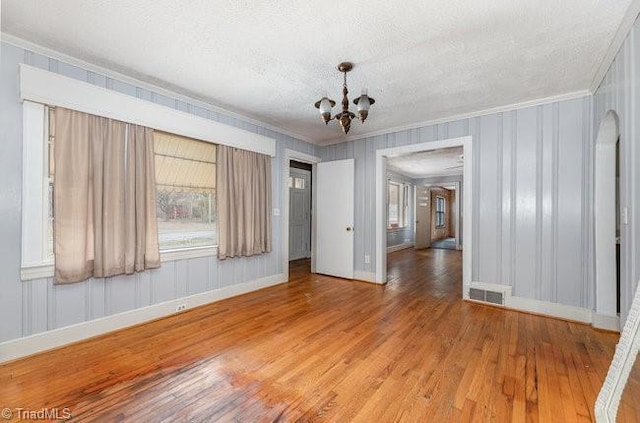 spare room featuring visible vents, wood finished floors, ornamental molding, and a chandelier