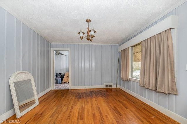 spare room with a chandelier, visible vents, a textured ceiling, and wood finished floors