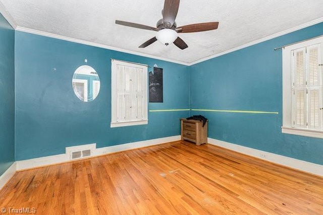 spare room featuring visible vents, ceiling fan, baseboards, ornamental molding, and wood finished floors