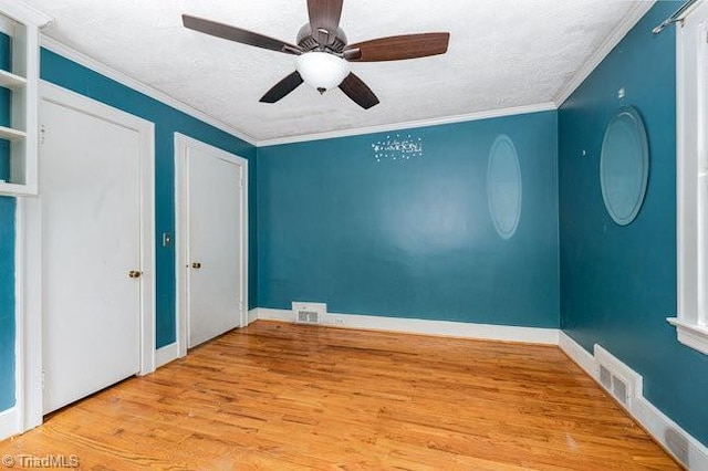 unfurnished bedroom with visible vents, multiple closets, ornamental molding, wood finished floors, and baseboards