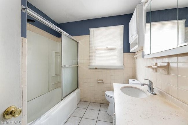 full bath featuring tile patterned floors, toilet, tile walls, bath / shower combo with glass door, and vanity