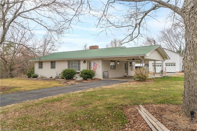 ranch-style house featuring a front yard, a chimney, metal roof, a carport, and driveway