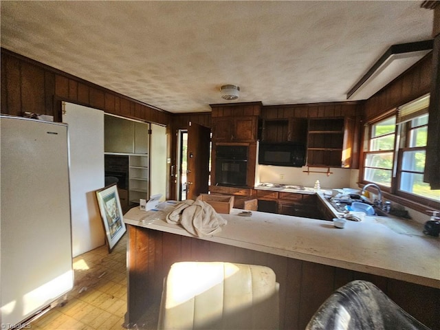 kitchen featuring a textured ceiling, sink, kitchen peninsula, wooden walls, and black appliances