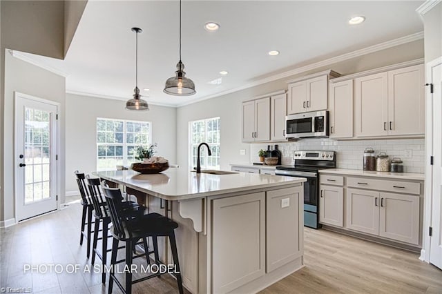 kitchen featuring sink, appliances with stainless steel finishes, hanging light fixtures, backsplash, and an island with sink