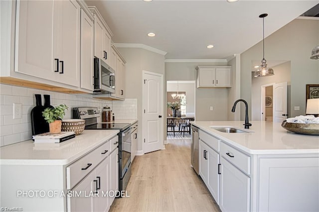 kitchen featuring appliances with stainless steel finishes, decorative light fixtures, an island with sink, sink, and white cabinets