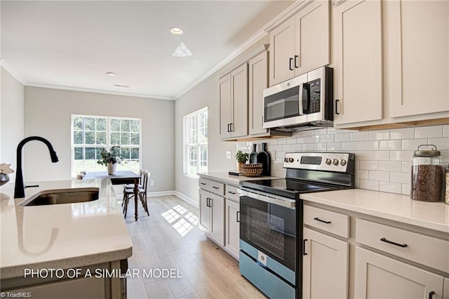 kitchen with sink, decorative backsplash, ornamental molding, stainless steel appliances, and light wood-type flooring