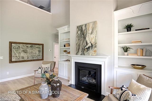 living area featuring built in shelves, light hardwood / wood-style floors, and a towering ceiling