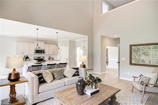 living room featuring a towering ceiling, ornamental molding, and light hardwood / wood-style flooring