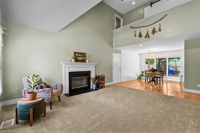 living room featuring carpet, baseboards, visible vents, a fireplace with flush hearth, and high vaulted ceiling