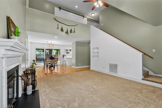 living area with stairs, visible vents, ceiling fan, carpet floors, and baseboards