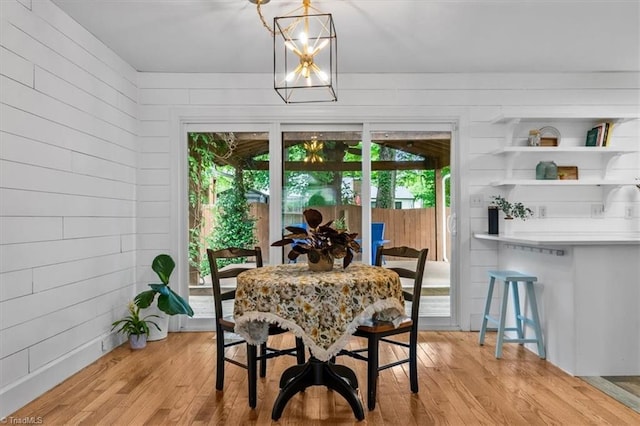 dining room featuring a wealth of natural light, light wood-style floors, wooden walls, and an inviting chandelier