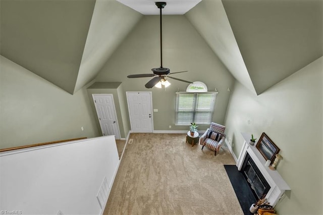 living area with carpet flooring, a ceiling fan, a fireplace with flush hearth, baseboards, and vaulted ceiling