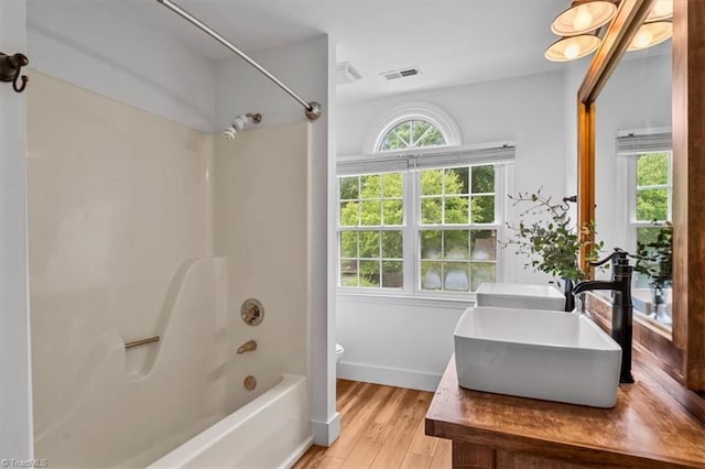 full bathroom with toilet, wood finished floors, a sink, visible vents, and shower / bathtub combination