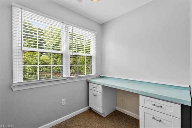 unfurnished office with built in desk, dark colored carpet, and baseboards