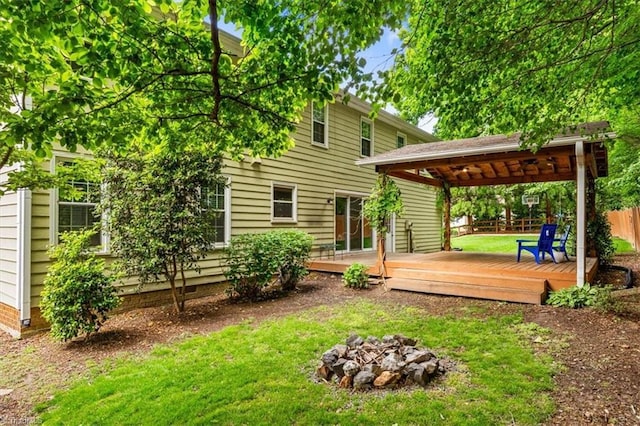 rear view of house with a lawn, a deck, a fire pit, and fence