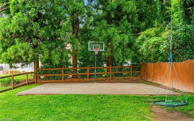 view of basketball court with a yard and fence