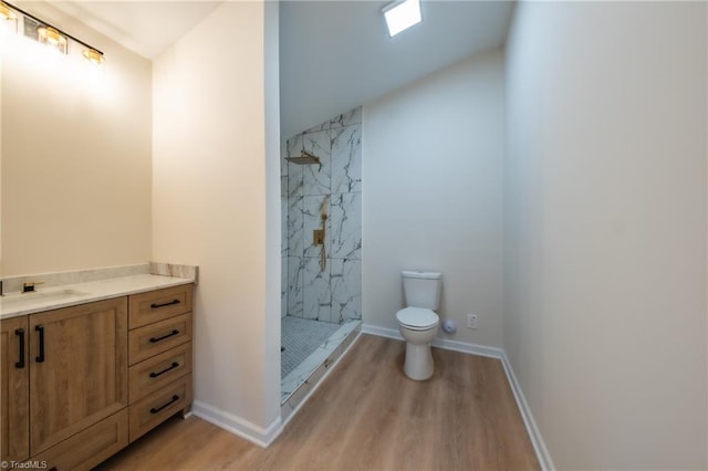 bathroom featuring a tile shower, vanity, vaulted ceiling, wood-type flooring, and toilet