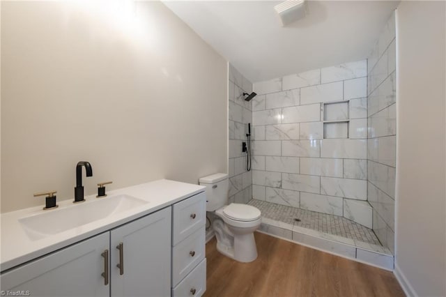 bathroom featuring tiled shower, wood-type flooring, vanity, and toilet