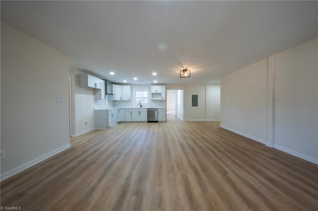 unfurnished living room featuring sink, electric panel, and light hardwood / wood-style flooring