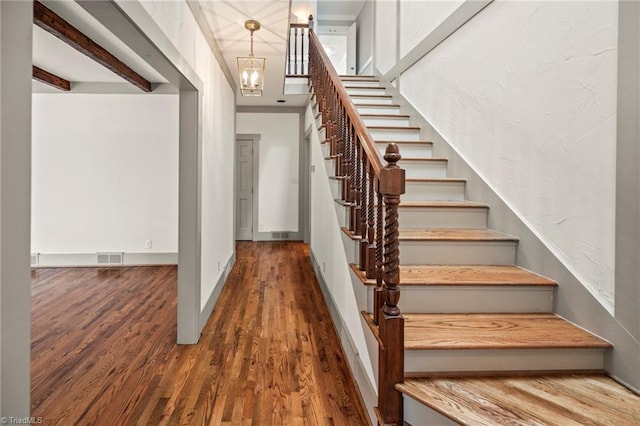 stairway with a chandelier, wood finished floors, visible vents, and baseboards