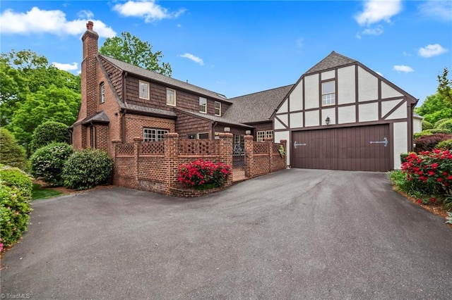 tudor house featuring a chimney, brick siding, a shingled roof, driveway, and an attached garage