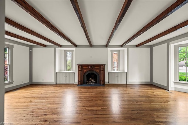 unfurnished living room with beam ceiling, wood finished floors, and a fireplace with flush hearth