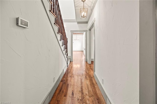 hall featuring an inviting chandelier, stairway, wood finished floors, and baseboards