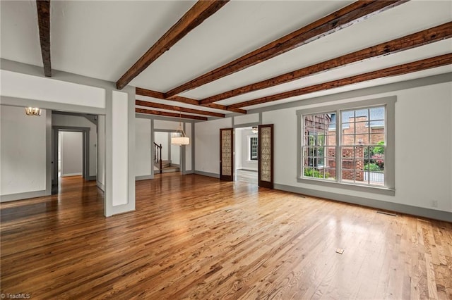 unfurnished living room with beam ceiling, wood finished floors, visible vents, and baseboards