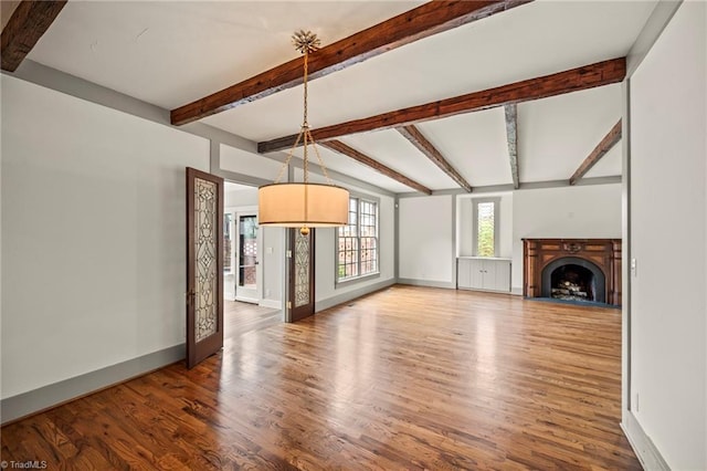 unfurnished living room featuring beam ceiling, wood finished floors, and baseboards