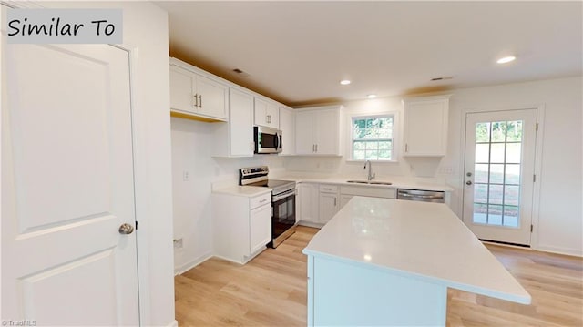 kitchen featuring white cabinetry, sink, appliances with stainless steel finishes, a kitchen island, and light wood-type flooring