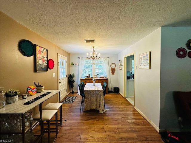 dining space with an inviting chandelier, hardwood / wood-style floors, and a textured ceiling