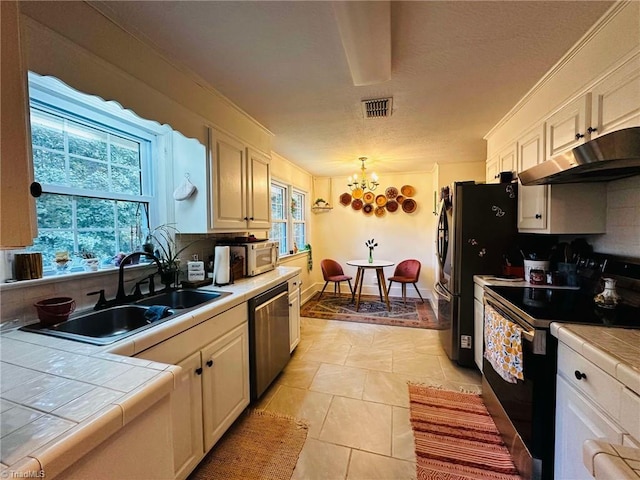 kitchen featuring tile countertops, sink, backsplash, appliances with stainless steel finishes, and decorative light fixtures