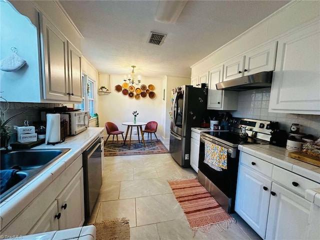 kitchen featuring stainless steel appliances, decorative light fixtures, decorative backsplash, white cabinets, and tile countertops