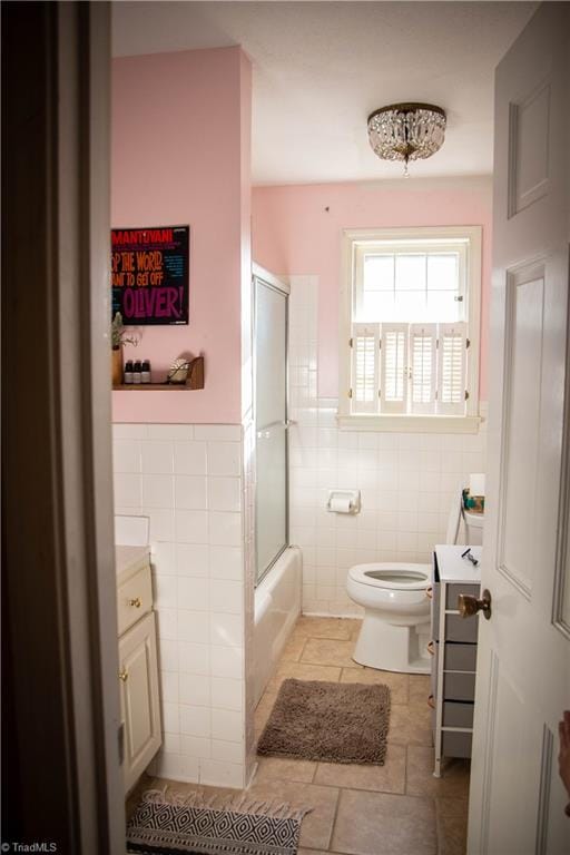 full bathroom featuring vanity, combined bath / shower with glass door, tile walls, and toilet