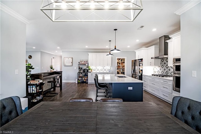 kitchen featuring appliances with stainless steel finishes, a kitchen breakfast bar, pendant lighting, a kitchen island with sink, and wall chimney range hood