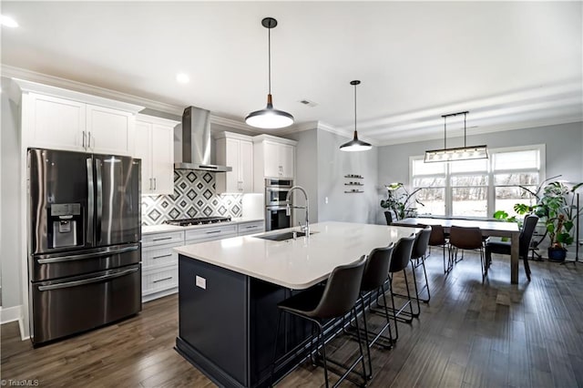 kitchen with wall chimney exhaust hood, sink, a center island with sink, stainless steel appliances, and white cabinets