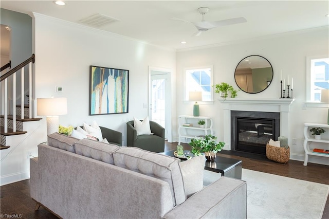 living room with ornamental molding, visible vents, dark wood finished floors, stairs, and a glass covered fireplace